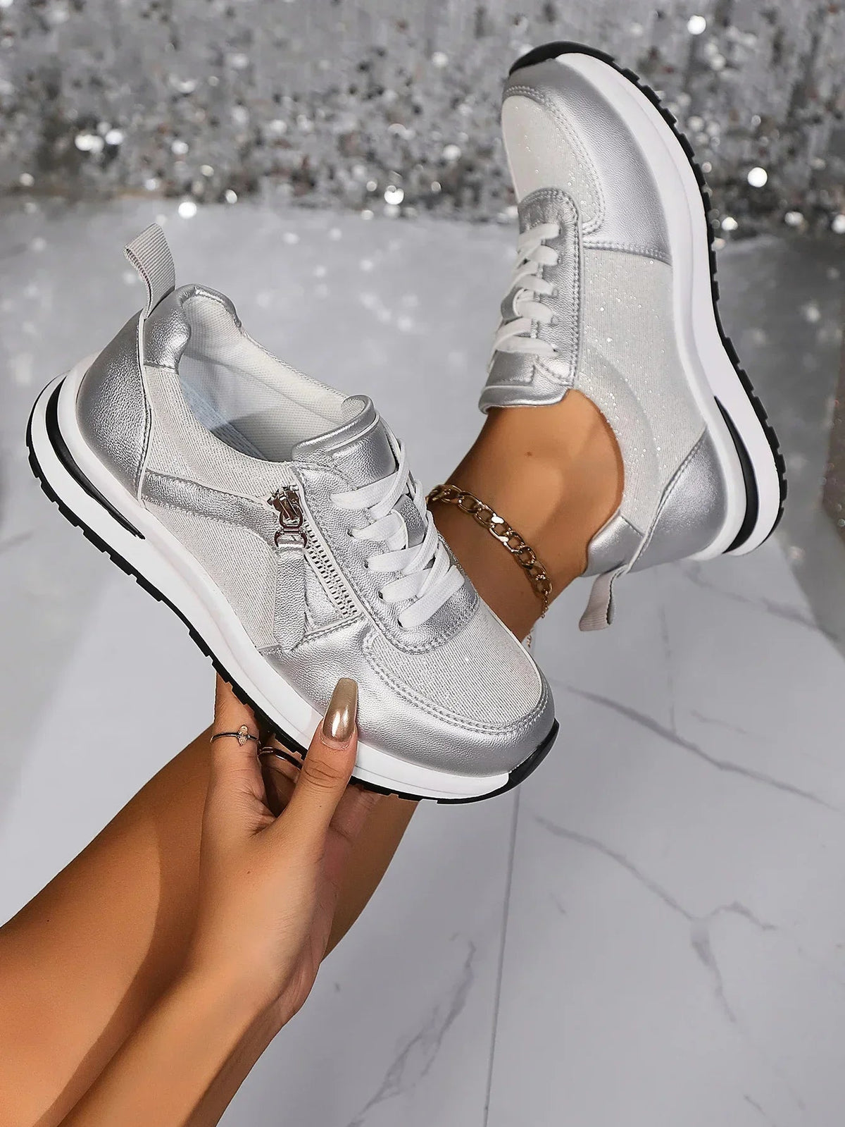 Silver platform lace-up sneakers with side zipper detail — angled view with model wearing and holding shoe